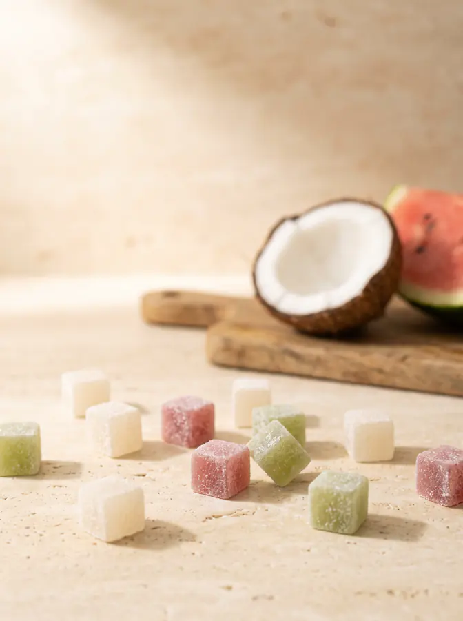 Coconut, watermelon and lime flavored gummies on cream stone, with fresh coconut and watermelon behind